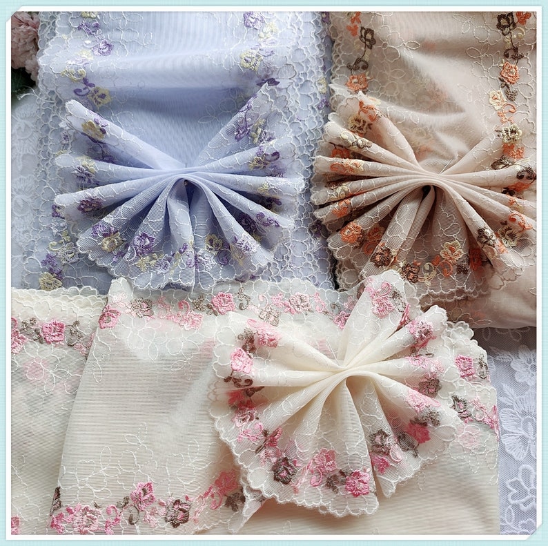 May include: Three pieces of delicate, embroidered fabric with floral patterns. Each piece is folded into a bow shape, showcasing the intricate lace details. The fabrics are in shades of light blue, peach, and cream.