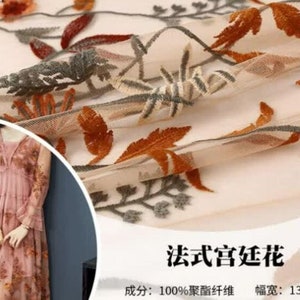 May include: Beige sheer fabric with embroidered floral designs in shades of orange, brown, and gray. The fabric is 100% polyester and has a width of 130 cm.