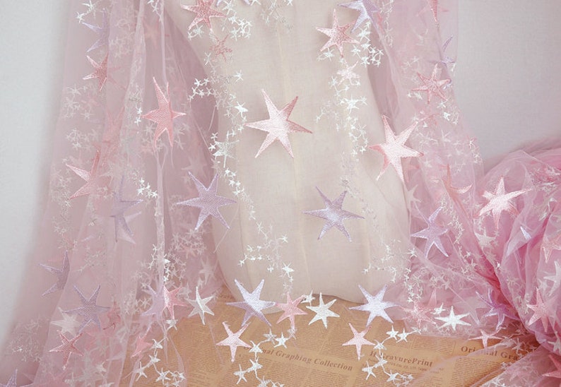 May include: Pink tulle fabric with embroidered white stars. The fabric has a gradient effect, with the stars fading from pink to white.