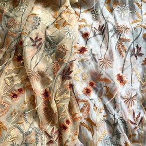 May include: Two pieces of sheer fabric with embroidered floral designs. One piece is beige with brown and gray embroidery, the other is white with brown and gray embroidery.