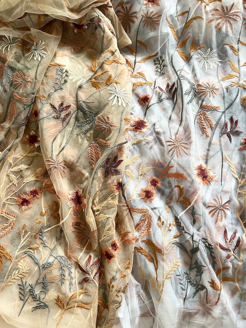 May include: Two pieces of sheer fabric with embroidered floral designs. One piece is beige with brown and gray embroidery, the other is white with brown and gray embroidery.