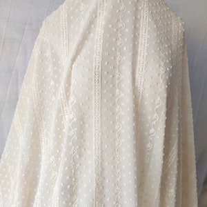 May include: White sheer fabric with a dotted and embroidered pattern. The fabric has vertical stripes of embroidery with a scalloped design.