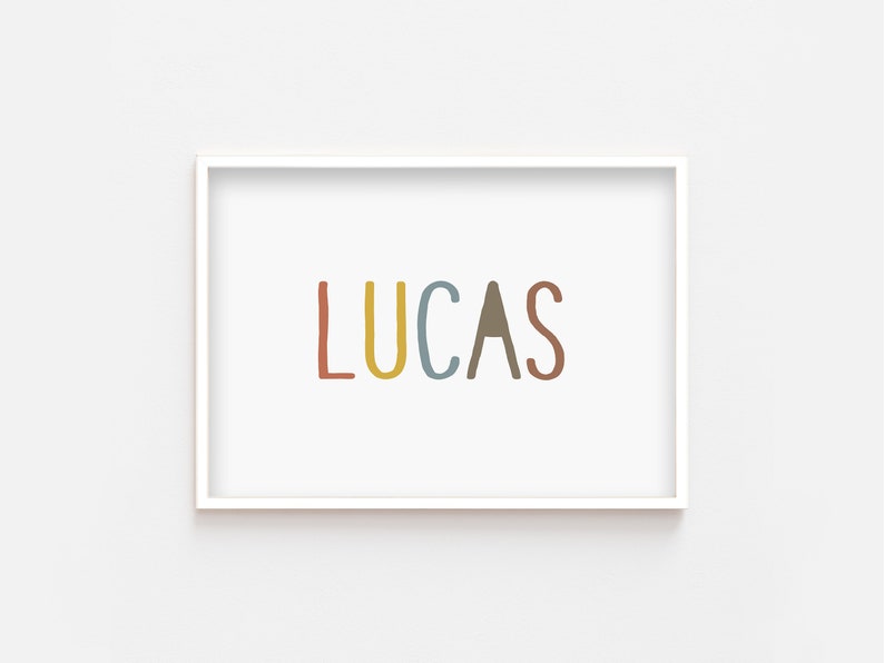 May include: A white framed print with the name "LUCAS" written in colorful, hand-drawn letters. The letters are red, yellow, blue, brown, and red.