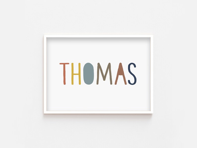 May include: A white framed print with the name "THOMAS" written in colorful, stylized letters. The letters are in shades of red, yellow, blue, brown, and gray.