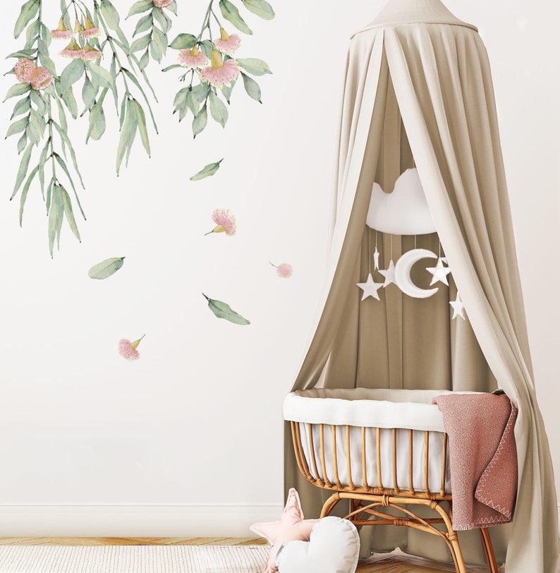 May include: A white canopy crib with a pink and green floral wall decal. The crib has a white mattress and a pink blanket. A white cloud mobile hangs above the crib.
