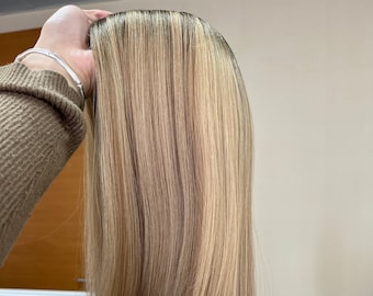 May include: A long, straight, light blonde wig with subtle highlights. The wig is styled with a centre parting and falls to the shoulders.