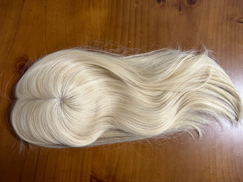 Puede incluir: Una peluca rubia con una base circular fina. El cabello es largo y ondulado, con una textura natural.