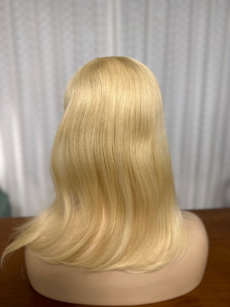 Puede incluir: Una peluca larga, lisa y rubia de cabello humano en una cabeza de maniqu&iacute;. La peluca est&aacute; peinada con un estilo simple y elegante, con el cabello cayendo recto hacia abajo de la espalda.