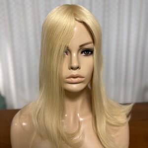 Puede incluir: Un topper de cabello humano rubio con un estilo recto y en capas. El topper est&aacute; en una cabeza de maniqu&iacute; y tiene un aspecto natural y realista.