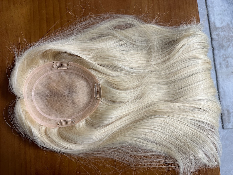 Puede incluir: Una pieza de pelo rubio con una base circular y clips para sujetarla. El pelo es largo y liso.