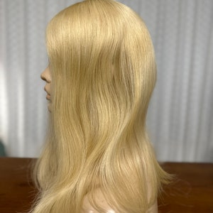 Puede incluir: Una peluca larga, lisa y rubia en una cabeza de maniqu&iacute;. La peluca est&aacute; peinada con raya lateral y capas.