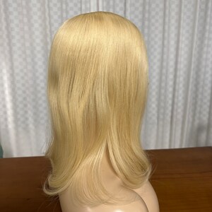 Puede incluir: Una peluca larga, lisa, de color rubio platino con una raya natural. La peluca est&aacute; peinada con una ligera onda en las puntas.