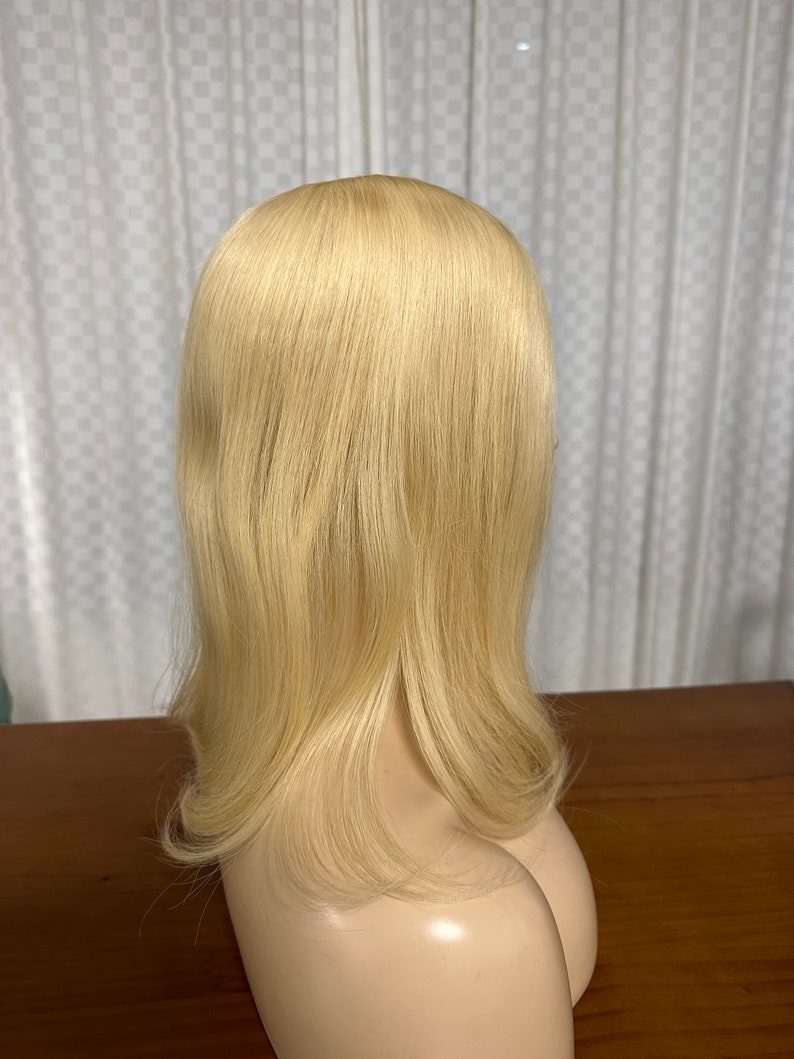 Puede incluir: Una peluca larga, lisa, de color rubio platino con una raya natural. La peluca est&aacute; peinada con una ligera onda en las puntas.