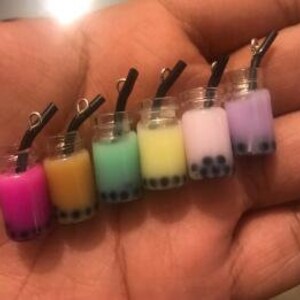 May include: Six miniature glass jars filled with different colored liquids and boba pearls. Each jar has a black straw and a silver charm attached to the top.