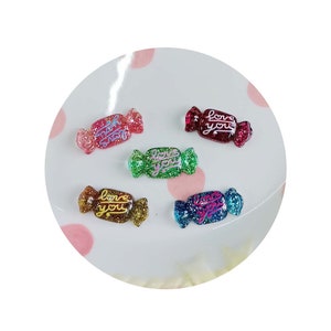May include: Five colorful candy-shaped resin charms with glitter and the words "Love You" written on them.