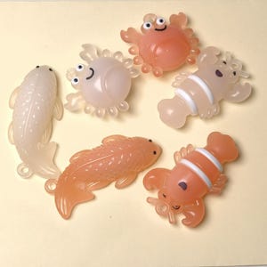 May include: A collection of translucent, colorful sea creature toys, including fish, crabs, and lobsters. The toys are in shades of peach, pink, and white, with cartoonish features. These small figurines are suitable for children's play or decorative purposes.