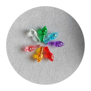 May include: A set of seven colorful Christmas light bulb tips in a rainbow pattern. The tips are arranged in a circle on a gray surface.