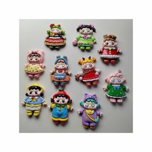 May include: A collection of ten small, colorful, flat-backed resin figurines depicting stylized characters in various outfits, including animal costumes, dresses, and overalls, featuring vibrant paint colors like red, green, blue, yellow, and purple.