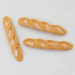 Puede incluir: Tres baguettes doradas con marcas blancas sobre una superficie blanca.