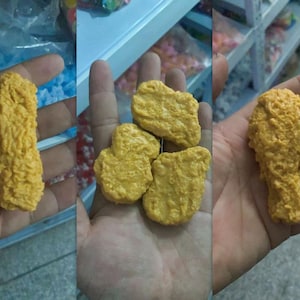 May include: Three hands holding various yellow, textured food items. The items resemble fried chicken and chicken nuggets. The food items are a bright yellow color and appear to be made of a solid material.
