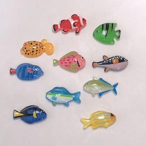 Puede incluir: Una colección de coloridas figuras decorativas de peces de diversas formas y tamaños. Los peces están pintados en colores brillantes, incluyendo rojo, verde, azul, amarillo y rosa, con patrones detallados. Las figuras probablemente están hechas de resina o un material similar.