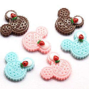 May include: Six colorful Mickey Mouse shaped cookie charms with a strawberry on top. The cookies are brown, pink, and blue.