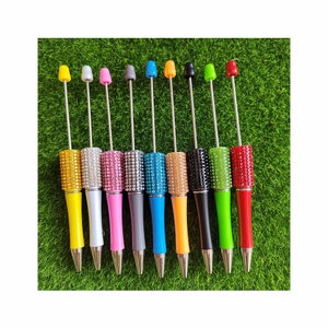 May include: Ten pens with rhinestones on the barrel. The pens are in various colours, including yellow, pink, blue, orange, green, and red.