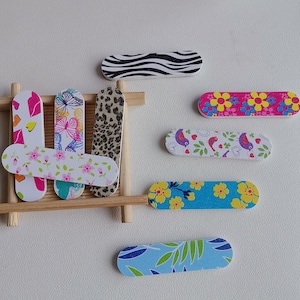 May include: A selection of patterned nail files in a variety of designs, including floral, butterfly, and animal prints. The files feature colours such as pink, blue, white, and brown. Some are arranged on a small wooden shelf.