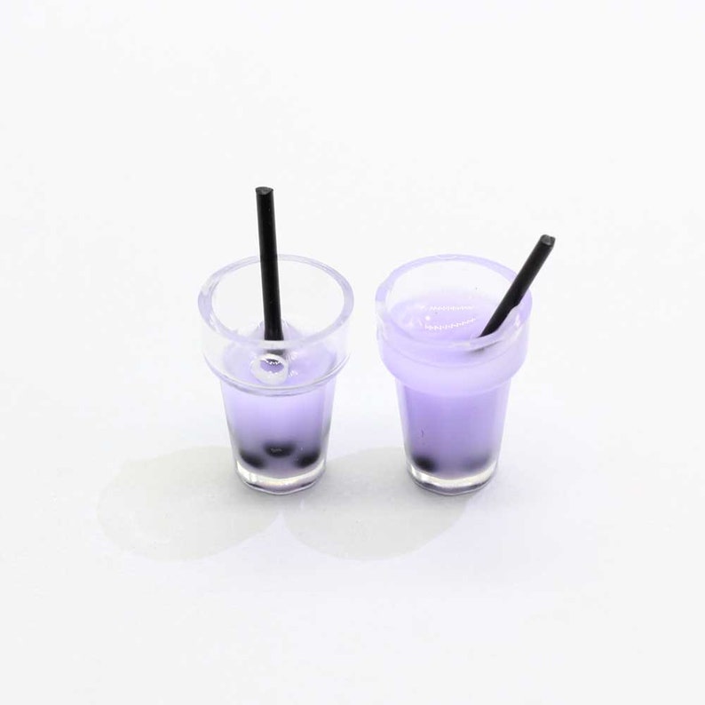 May include: Two miniature plastic cups filled with purple liquid and black boba pearls. Each cup has a black straw sticking out of the top.