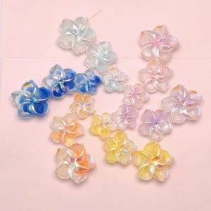 May include: A collection of iridescent flower-shaped embellishments in various colors, including blue, pink, yellow, and orange. The translucent petals catch the light, creating a shimmering effect. These decorative pieces are ideal for craft projects.