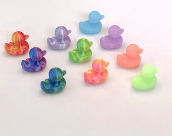 May include: A collection of small, colorful duck figurines in various shades including red, blue, green, and purple. The ducks have a textured, 3D-printed appearance and are arranged on a white surface. These decorative ducks are suitable for home decor or as collectibles.