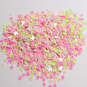 Puede incluir: Una mezcla de adornos de arcilla polimérica coloridos. La mezcla incluye pequeñas flores rosas con centros amarillos, hojas verde claro y formas de mariposas iridiscentes. Ideal para scrapbooking y otros proyectos de manualidades.