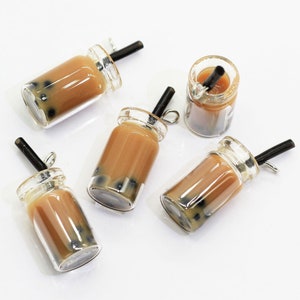May include: Five clear glass jars with brown liquid and black straws. The jars have a silver lid and are filled with brown liquid and black tapioca pearls.