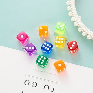 May include: Assortment of colourful dice charms with white dots. The dice are made of clear plastic and have a hole at the top for hanging.