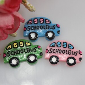 May include: Three miniature school bus figurines, one blue, one green, and one pink, with black outlines and white wheels. Each bus has the words "SCHOOL BUS" written on the side.