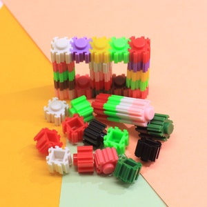 May include: A set of colourful plastic building blocks in various shapes and sizes. The blocks are arranged in a frame shape with some blocks scattered around it. The blocks are red, green, white, pink, yellow, purple, and brown.