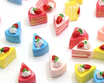 May include: Assortment of miniature cake slices with strawberry and whipped cream toppings. The cakes are in various colors, including pink, blue, yellow, and white.