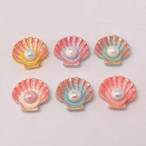 May include: Six iridescent seashell-shaped embellishments with a pearl in the center. The shells have a variety of colors, including yellow, pink, green, and blue. The pearls are white and have a shiny finish. These are likely used for crafts or jewelry making.