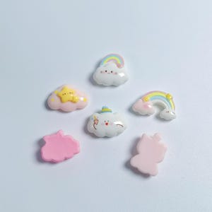 May include: A collection of six small resin charms featuring pastel-colored clouds, rainbows, and stars. The pieces include a cloud with a rainbow, a pink cloud with a yellow star, a cloud holding an ice cream cone, and solid pink shapes.