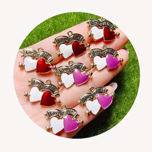 May include: A set of seven gold-tone charms featuring two interlocking hearts with a banner that reads "Lovely Girl". The hearts are enamelled in white and red or white and pink.