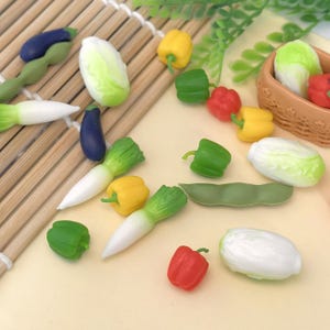 May include: Miniature vegetable models including green and red peppers, yellow peppers, aubergines, and cabbages. The vegetables are arranged on a bamboo mat and a light-coloured surface.