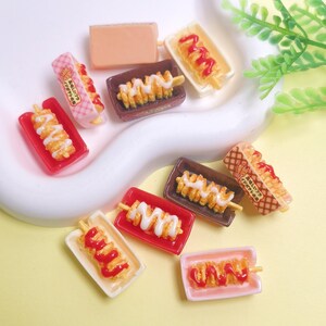 May include: Miniature food items including spiral-cut fries on skewers, hot dogs, and a rectangular block. The fries are drizzled with white and red sauces, presented in small trays. Some items have Japanese text on the packaging.
