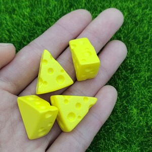 May include: Four yellow cheese-shaped dice with a textured surface. The dice are on a hand.