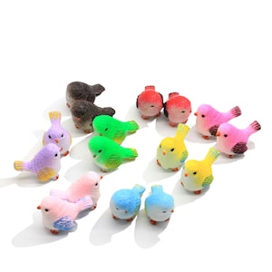 May include: A set of twelve miniature bird figurines in various colours, including pink, purple, green, yellow, blue, and red. The birds are made of a smooth, textured material and are perfect for adding a touch of whimsy to a miniature garden or fairy garden.