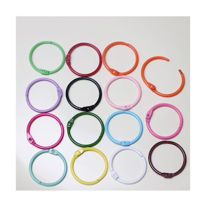 May include: Assortment of 15 colourful metal binder rings in various sizes. The rings are in shades of green, red, orange, purple, black, blue, pink, yellow, and brown.