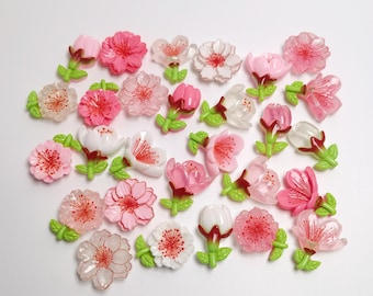 以下が含まれることがあります： ピンク、白、透明など様々な色の人工花のコレクション。花には緑色の茎と葉があります。つぼみから満開まで、さまざまな開花段階の花があります。