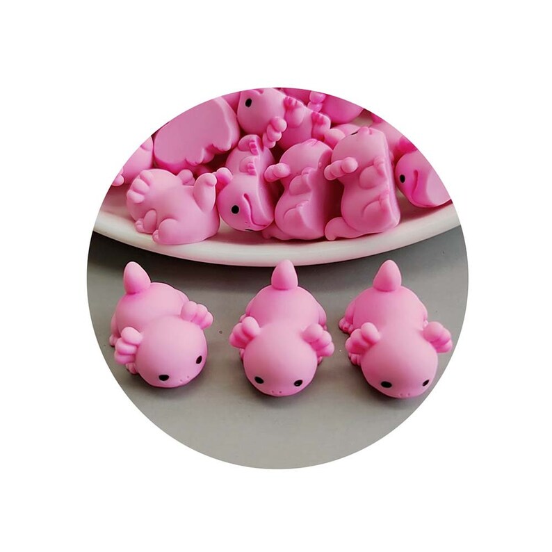 May include: A group of pink axolotl figurines, some are stacked on a white plate, while others are arranged in a row on a grey surface.