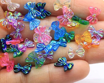 May include: Assortment of iridescent plastic bow embellishments in various colors, including blue, green, pink, and orange. The bows are small and have a shiny, reflective finish.