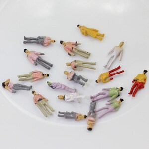 Op de afbeelding: Een verzameling van miniatuur plastic figuren in verschillende poses en kleuren, die mensen voorstellen. De figuren zijn geschilderd in tinten roze, geel, groen, rood, wit en grijs. Ze zijn ideaal voor modeltreinbanen of andere miniatuur sc&egrave;nes.
