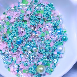 May include: A bowl filled with green, pink and white sprinkles, beads and sequins. The sprinkles are shaped like four-leaf clovers.